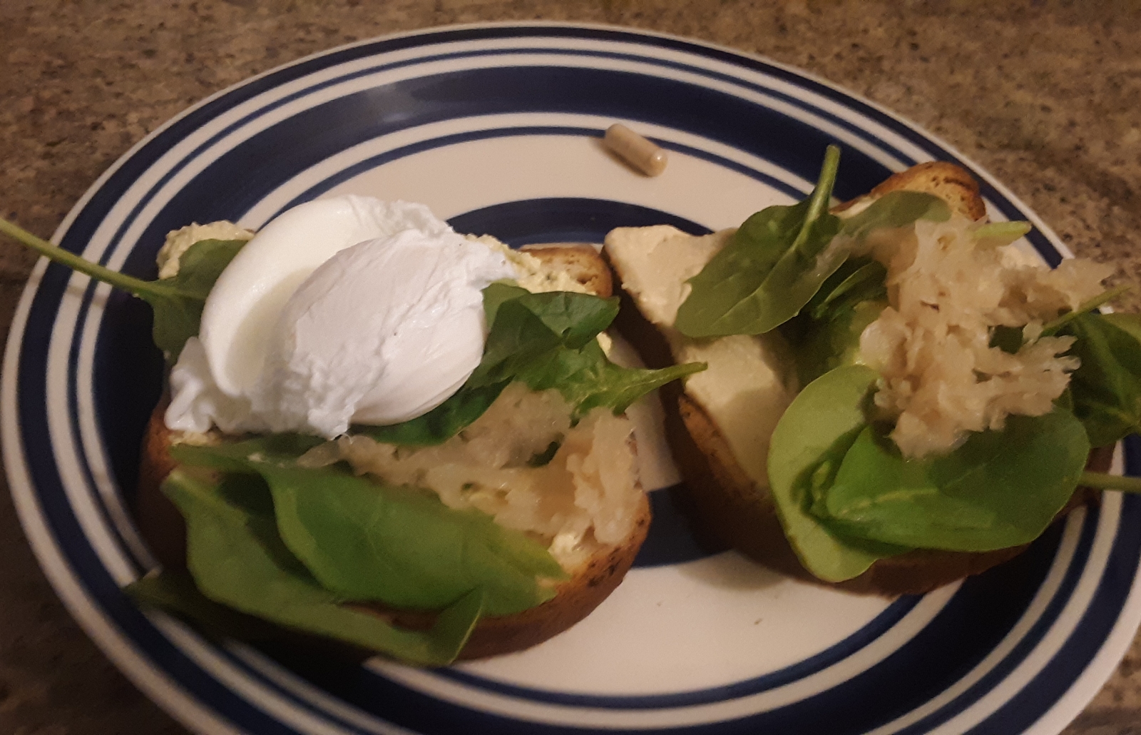Living well in the 21st century - Limassol, Cyprus - gluten free bread with Sauerkraut, poached egg, sliced avocado, hummus and spinach on a blue plate. 