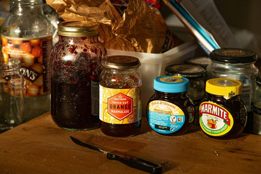 Living well in the 21st century-Limassol, Cyprus. A picture of four glass containers. A marmite container, and another reduced salt marmite container. Other two glass jars contain jam. Also, there is a knife on a brown table. 
